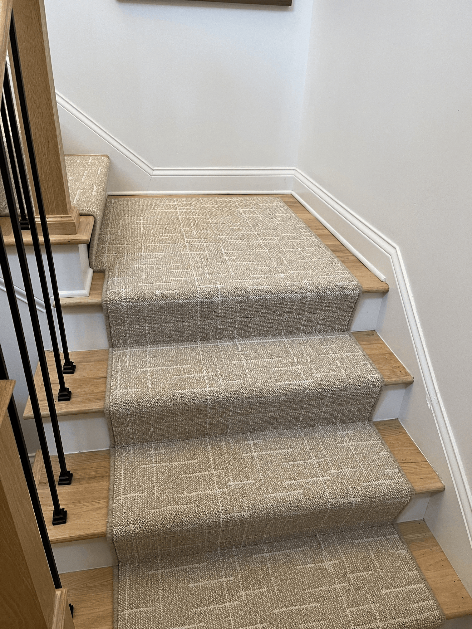 Carpeted staircase with wooden steps and white walls, viewed from the bottom.