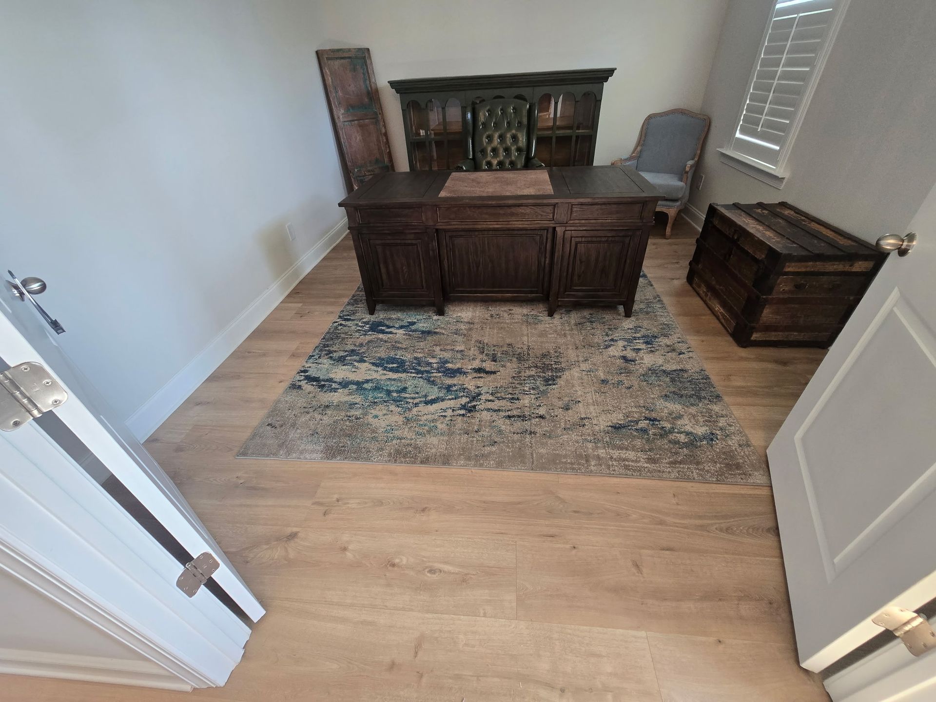 Empty room with wooden desk, cabinet, side table, and patterned rug on hardwood floor.