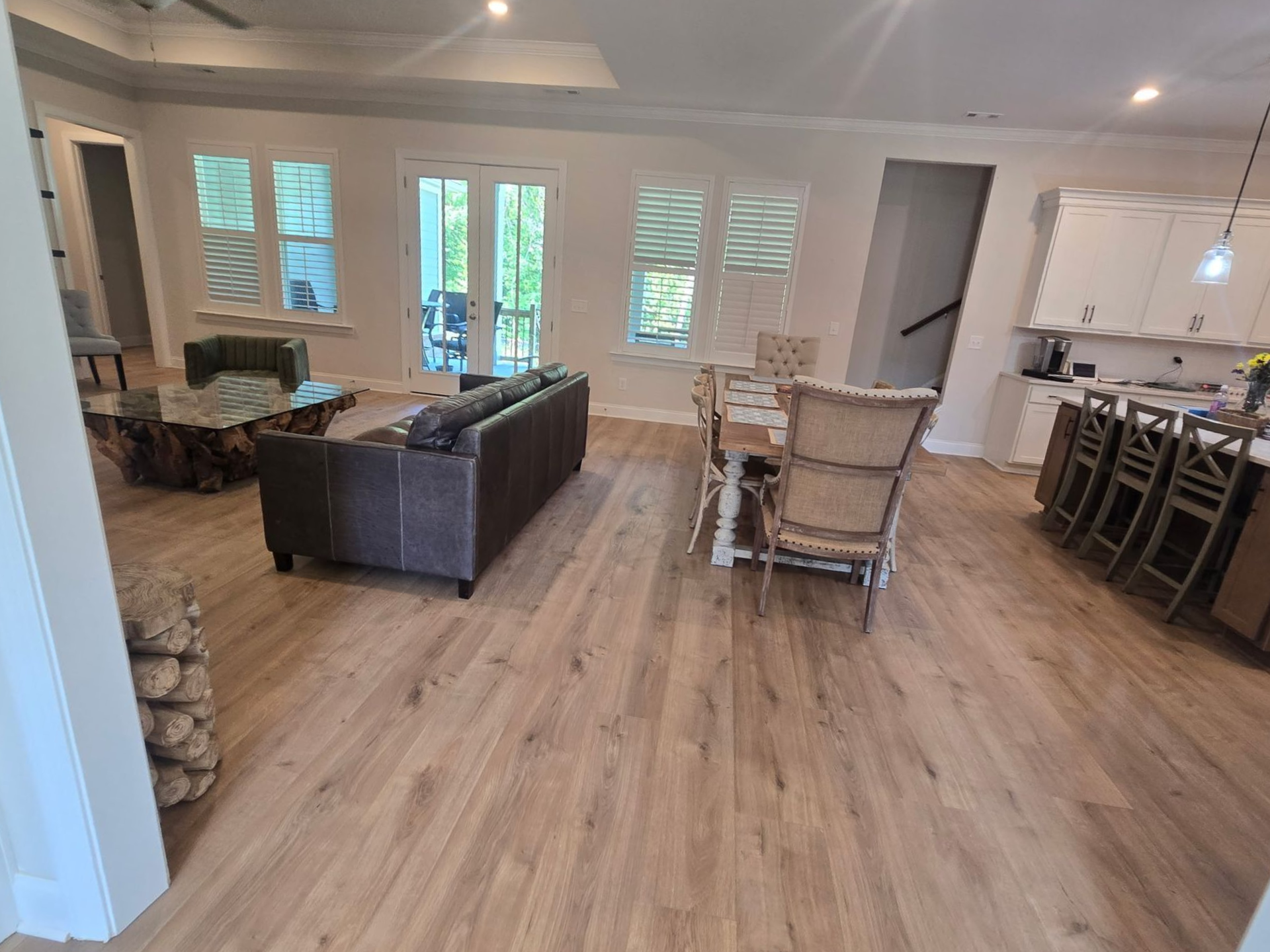 Open living room with dark sofa, dining table, bar stools, and kitchen in the background.