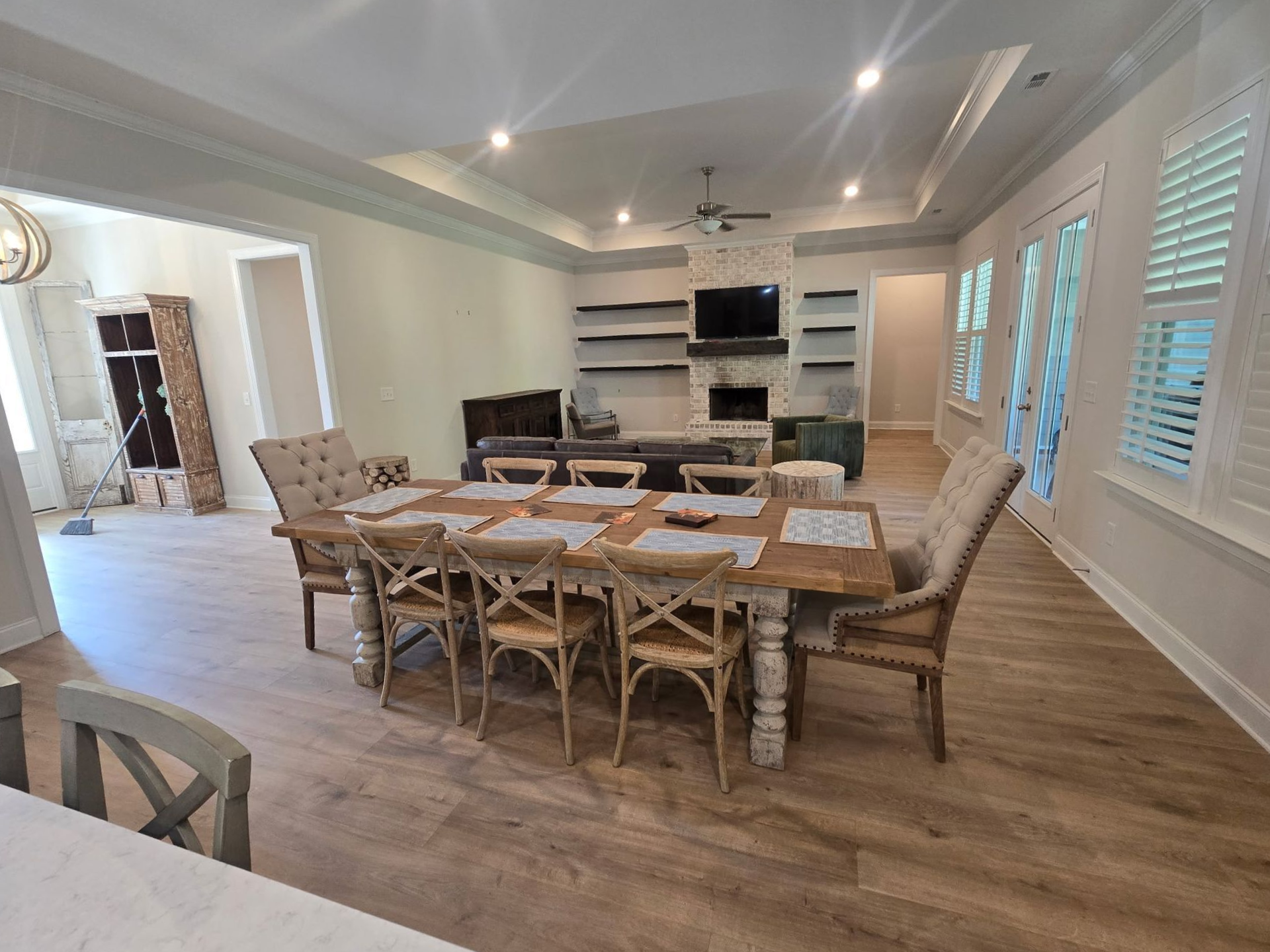 Bright dining room with a long wooden table, woven chairs, and built-in shelves by large windows.