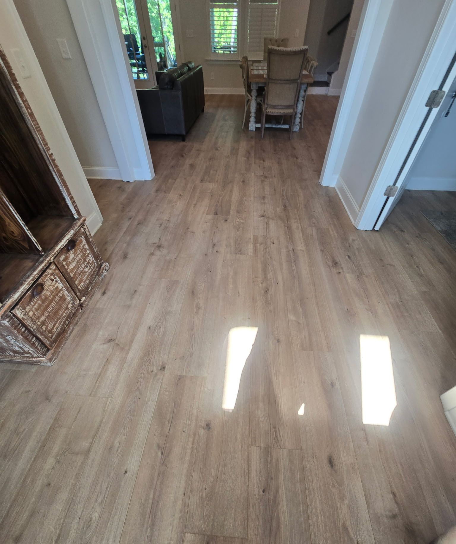 Hallway with light wood floors, white walls, and chairs at the far end near a window.
