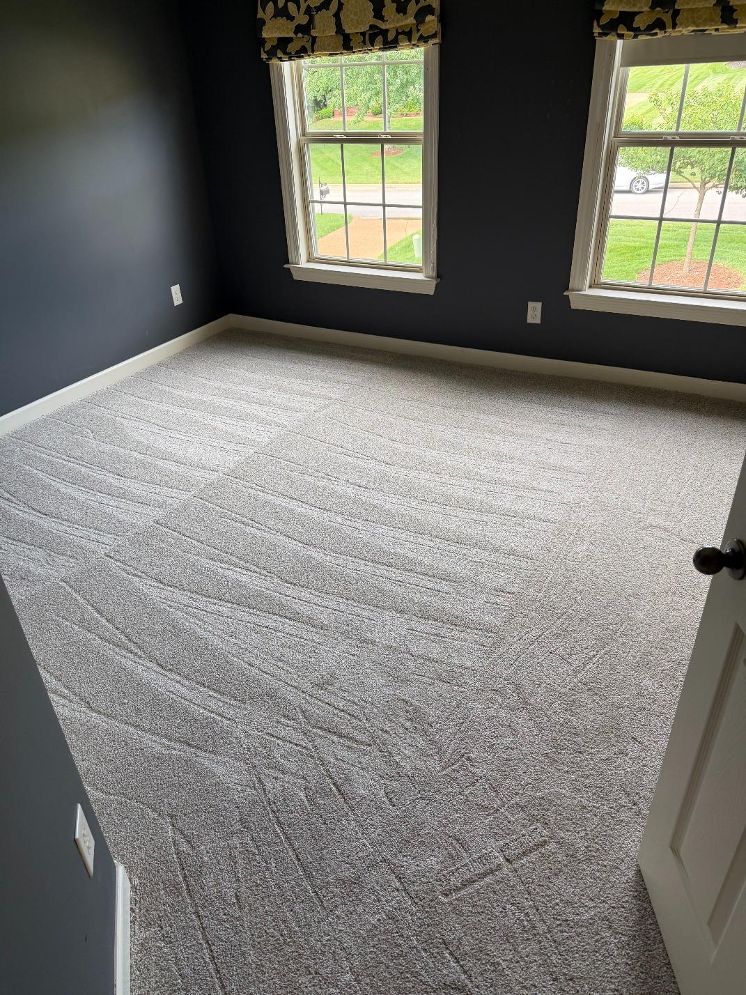 Empty bedroom with gray carpet, dark walls, and two windows letting in daylight.