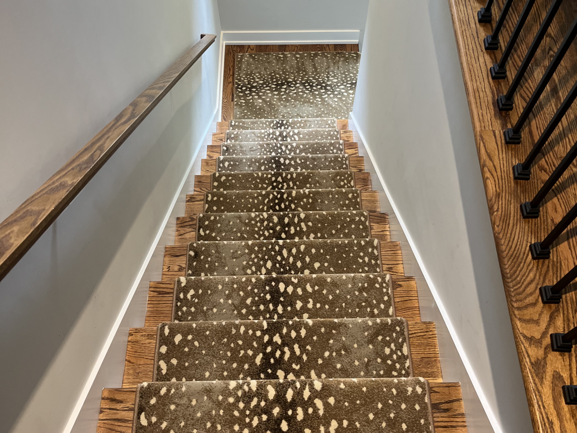 Staircase with speckled carpet, white walls, and wooden handrails viewed from the top.