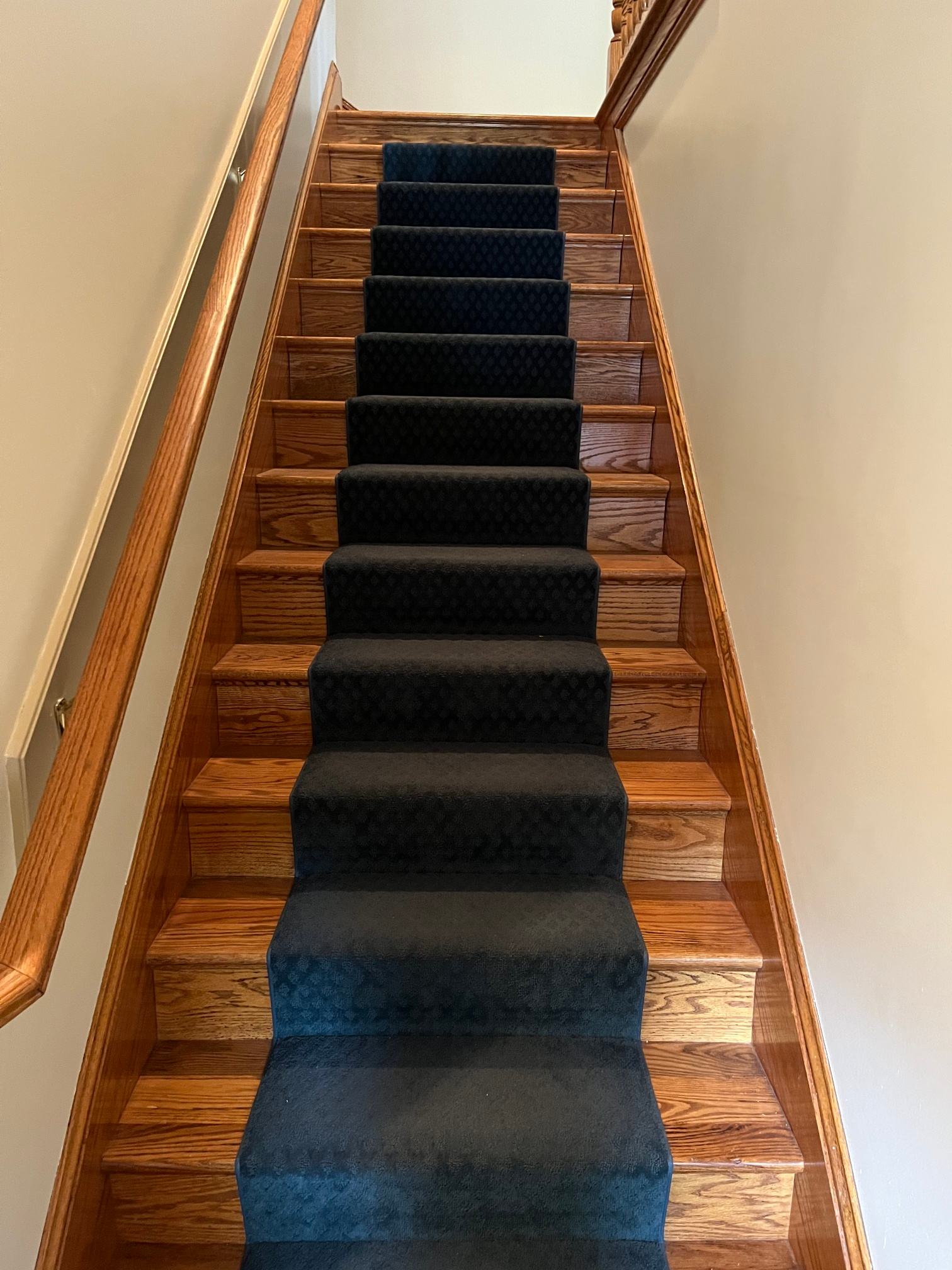 Narrow wooden staircase with a dark carpet runner leading upward between cream walls