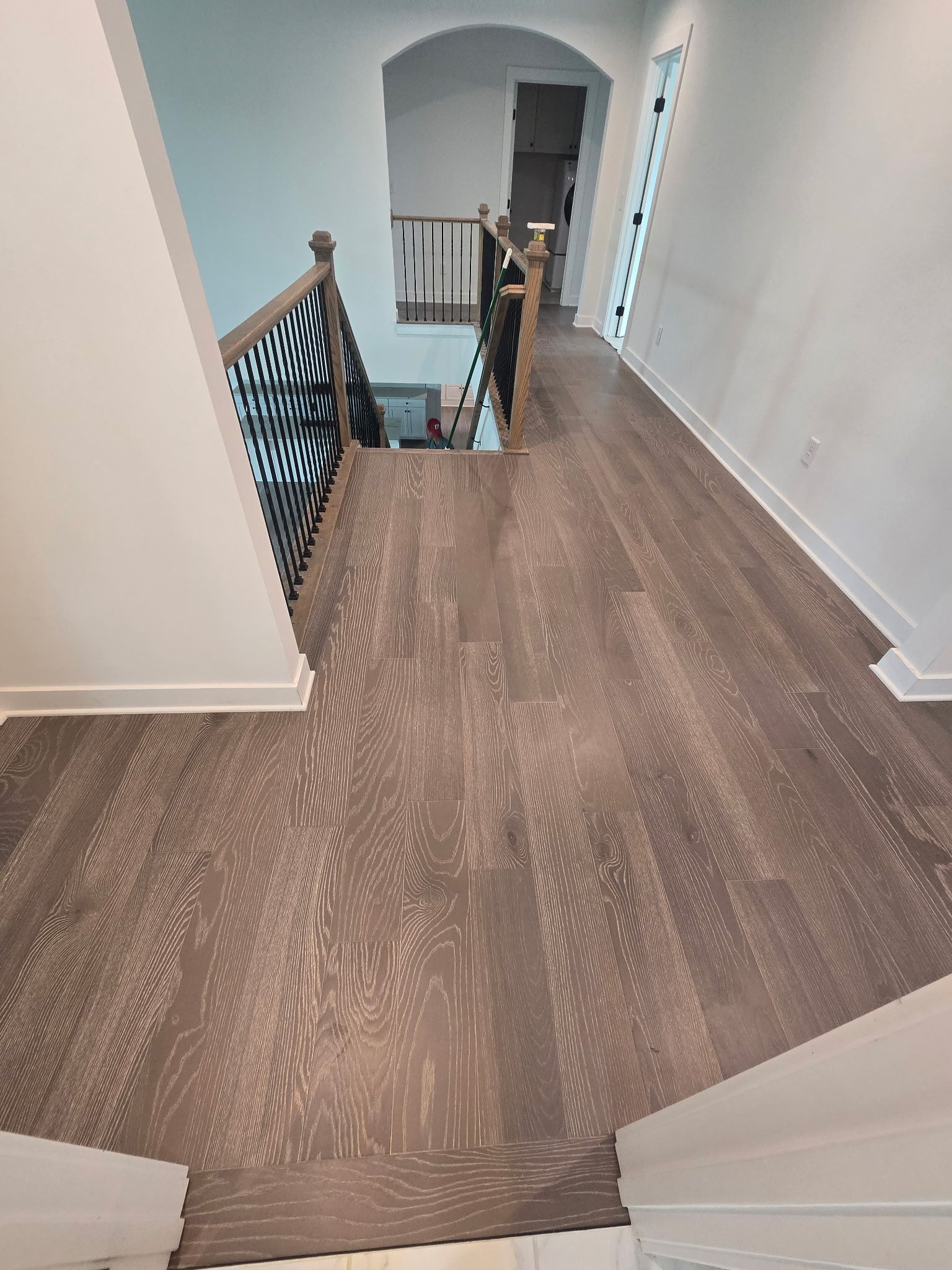 Hallway with wood flooring and staircase railing leading to a doorway at the far end.