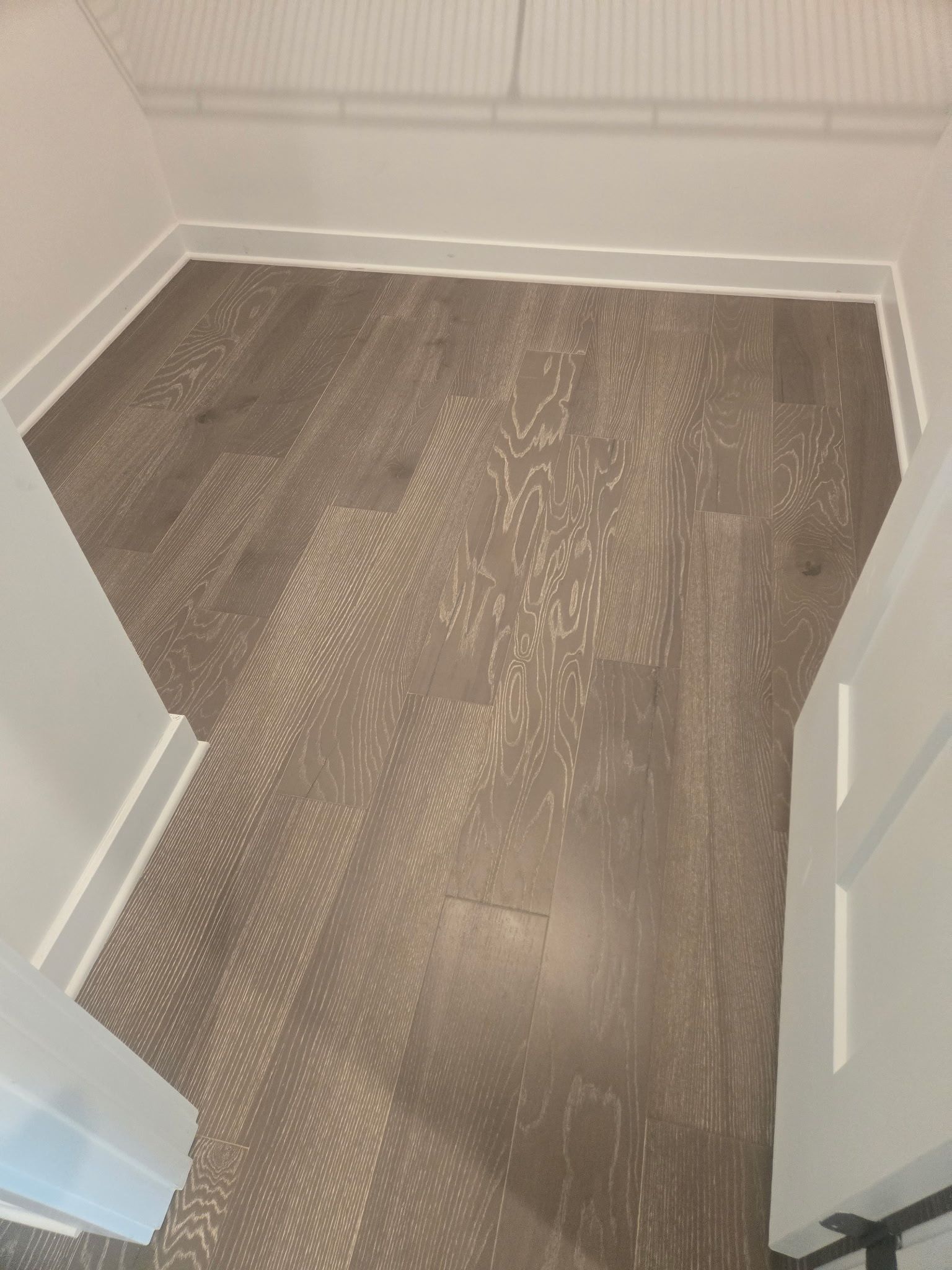 Empty hallway corner with gray wood-look flooring and white walls, viewed through a partially open door