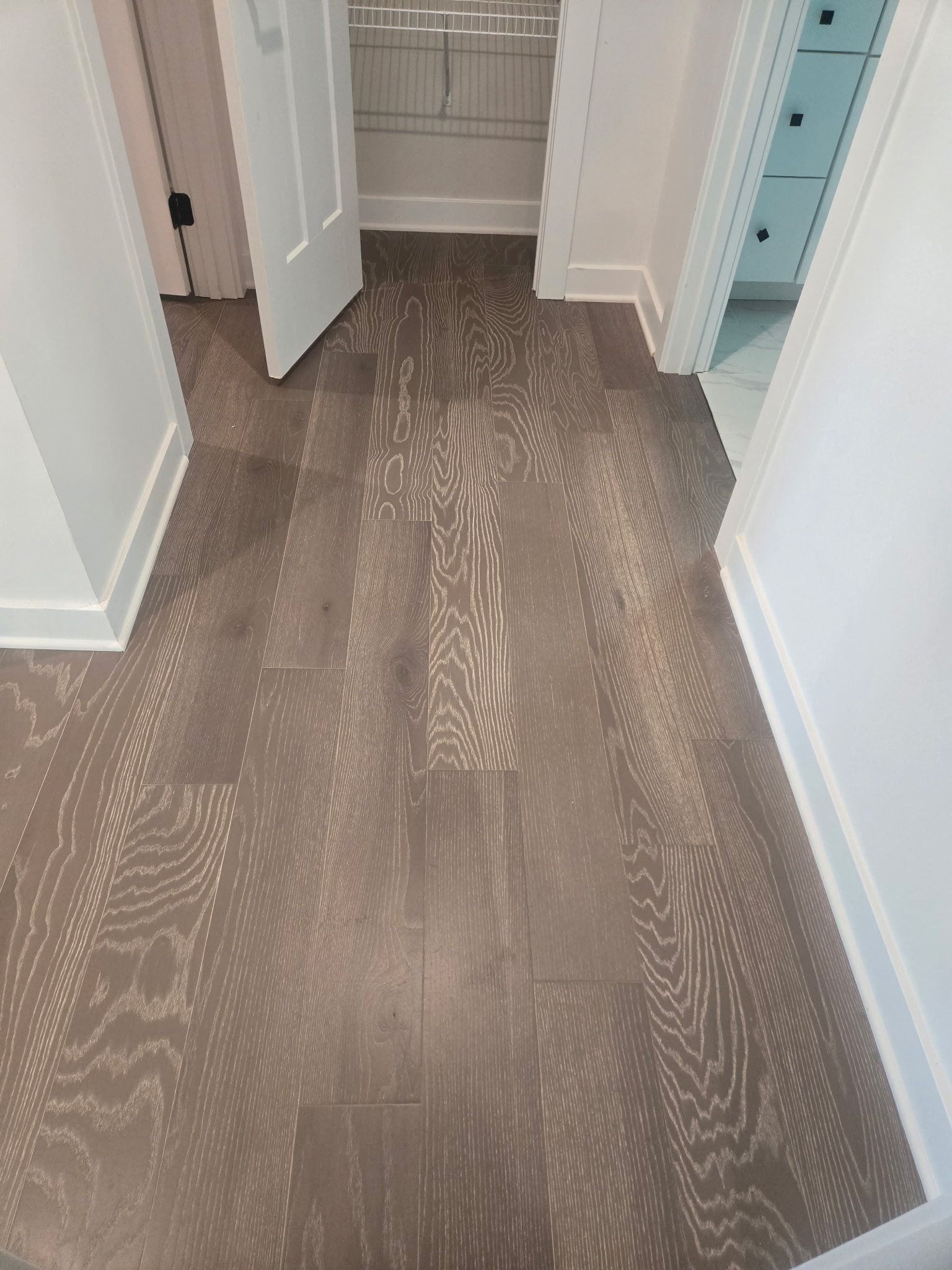 Empty hallway with gray wood flooring, open closet door, and built-in blue drawers.