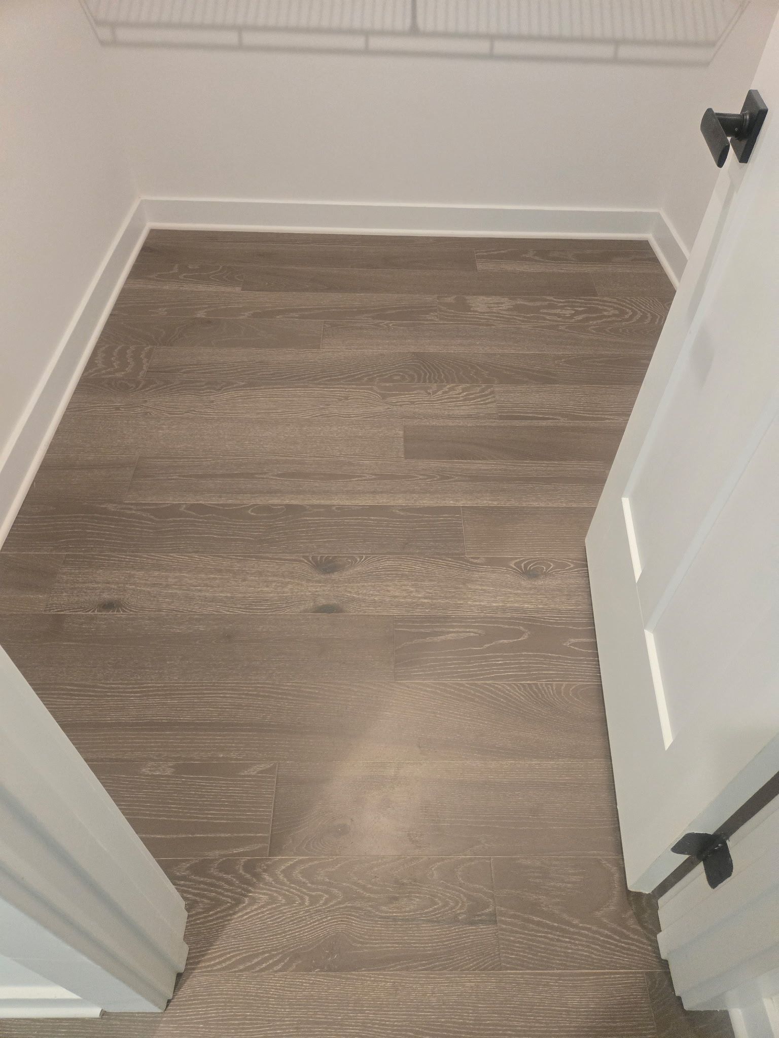 Small empty hallway with wood flooring and white walls, viewed through an open doorway.