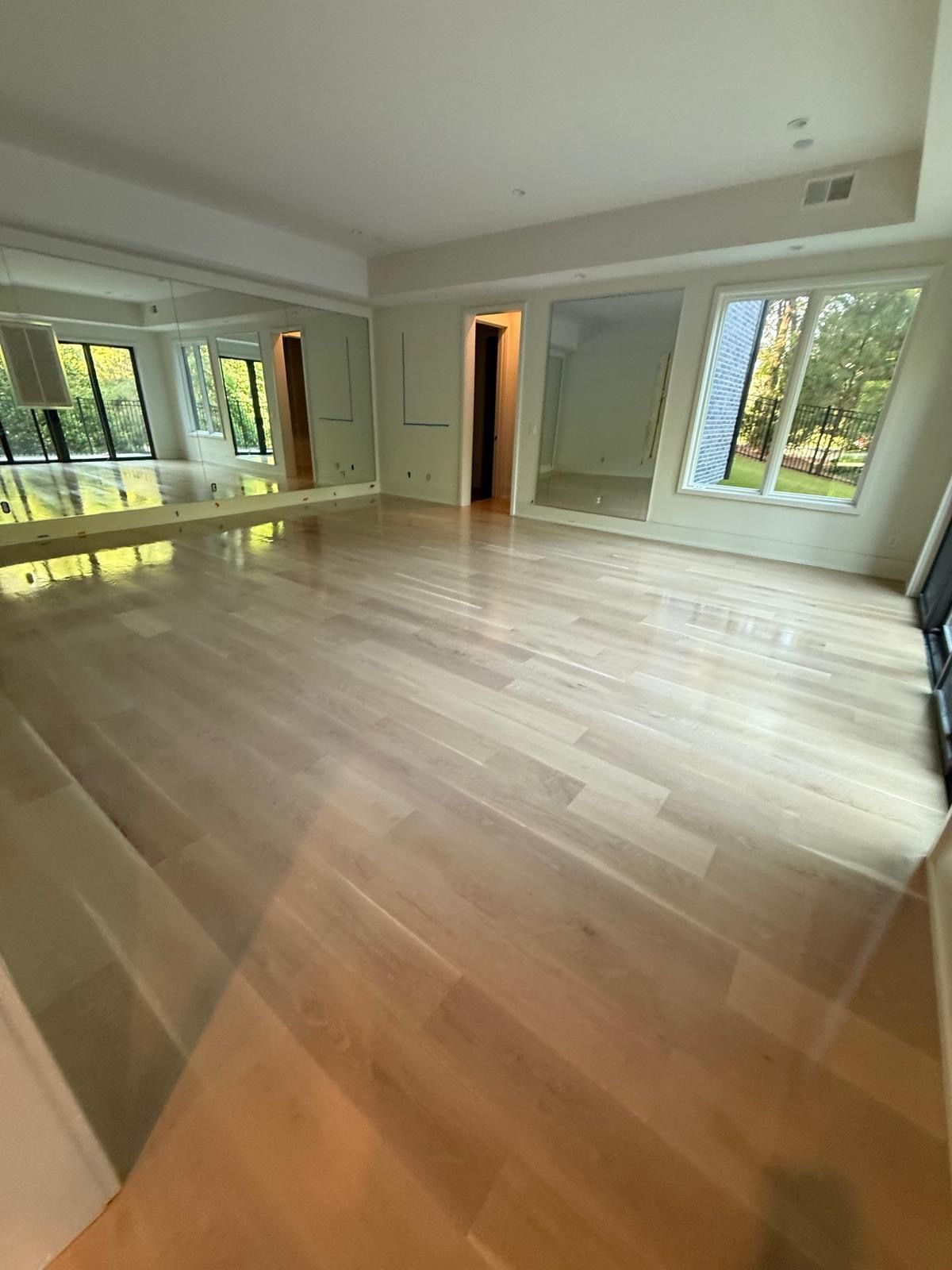 Empty living room with light wood floors, large windows, and an open doorway