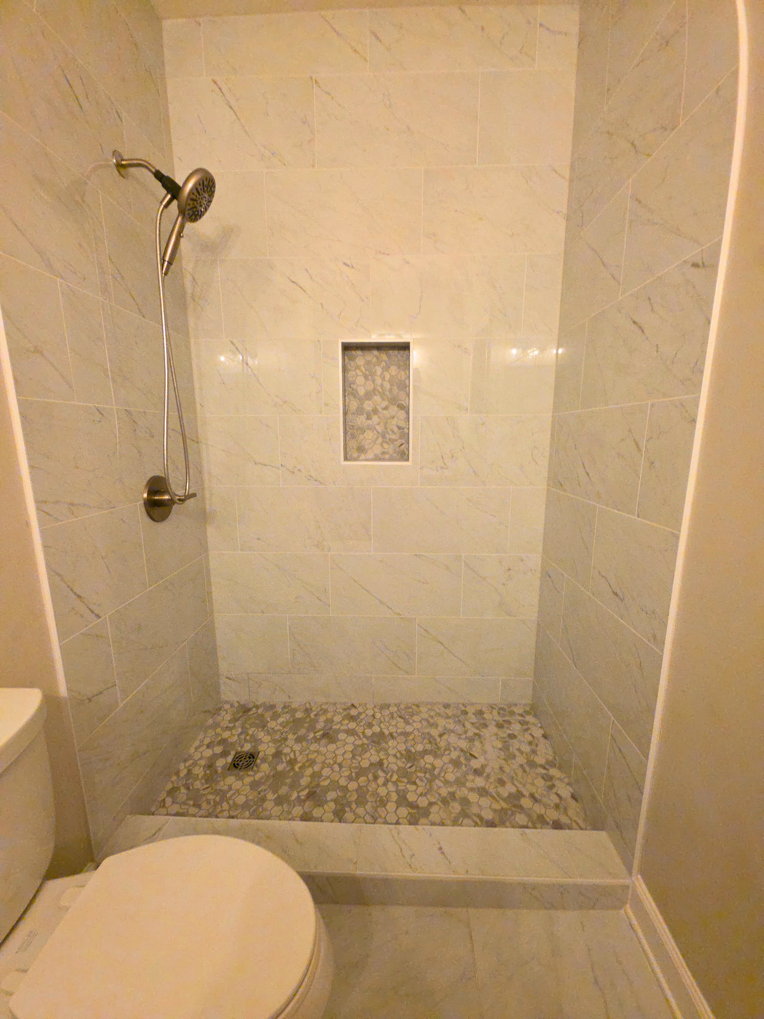 Bathroom shower with beige tile walls, pebble floor, and built-in niche