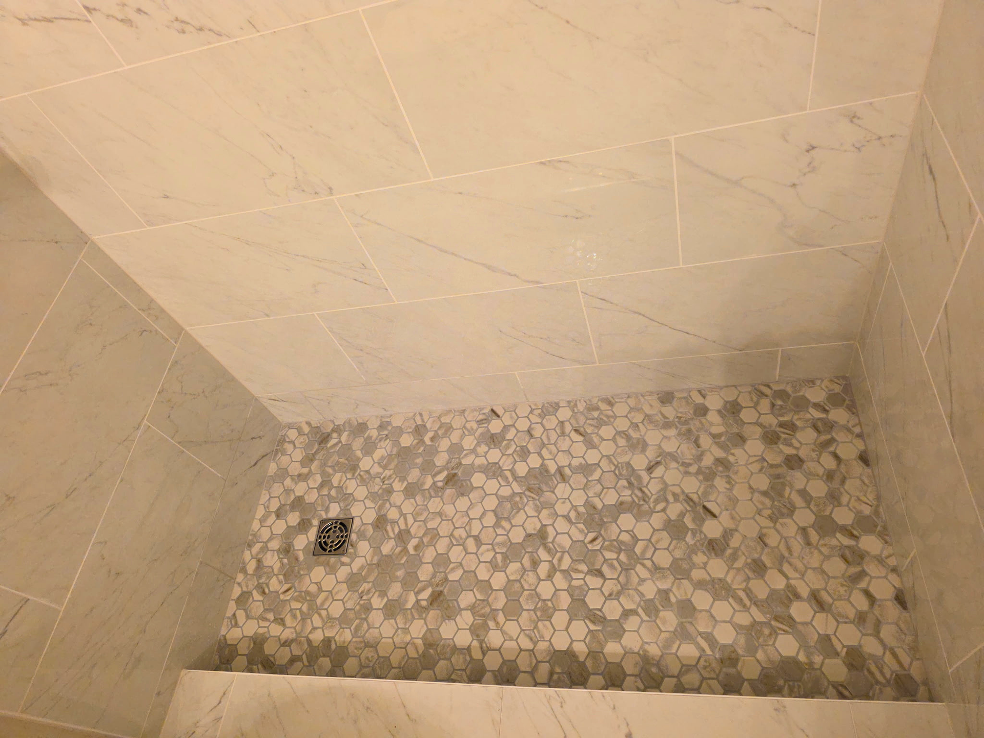 Small tiled shower stall with beige walls and pebble-patterned floor, viewed from above.