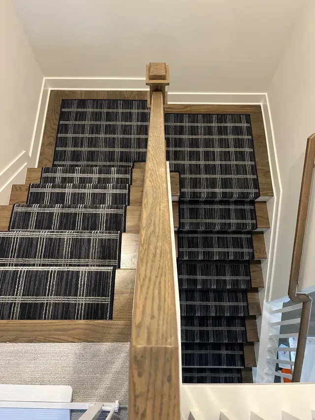 Top-down view of black-carpeted stairs split by a central wooden divider in a beige interior.