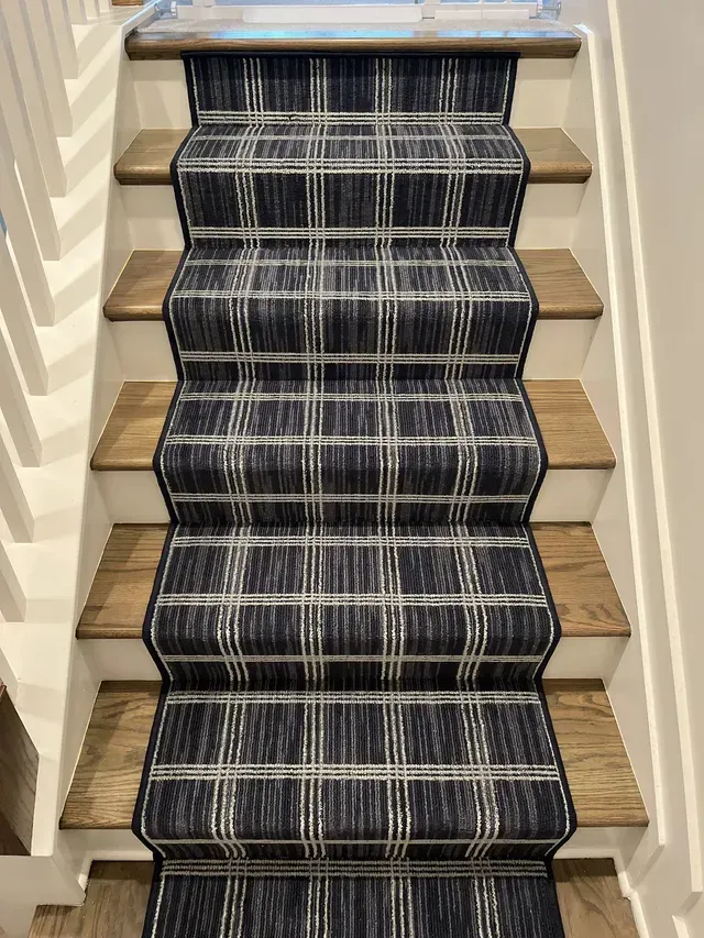 Carpeted staircase with dark striped runner and light wood steps, viewed from below.