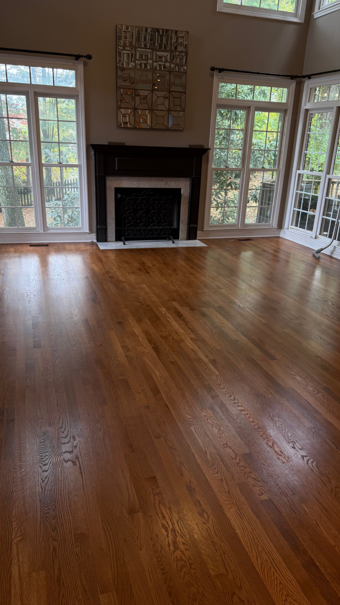 Empty living room with hardwood floors, a fireplace, and large windows letting in daylight
