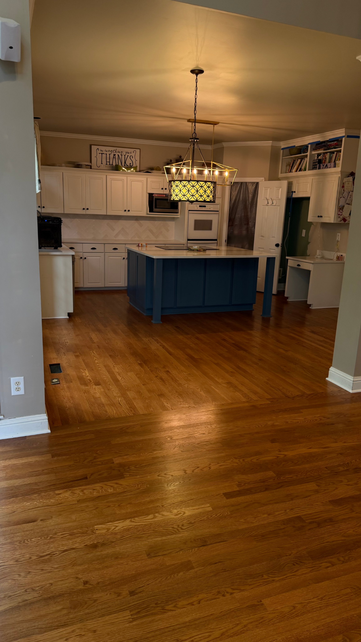 Open kitchen with white cabinets, blue island, hanging light, and wood floors