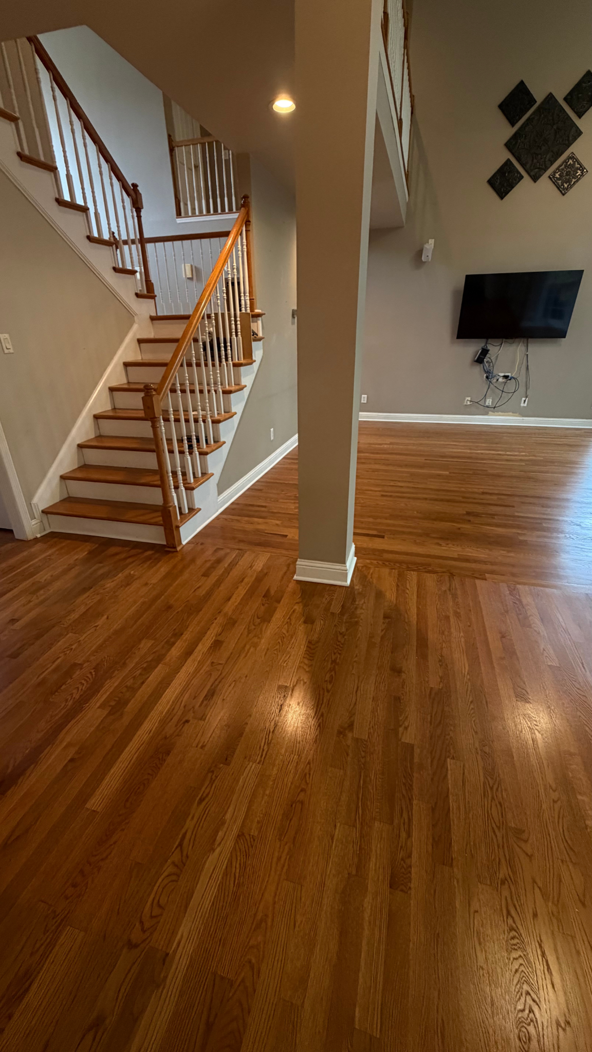 Empty living room with wood floors, staircase on the left, and a wall-mounted TV on the right.