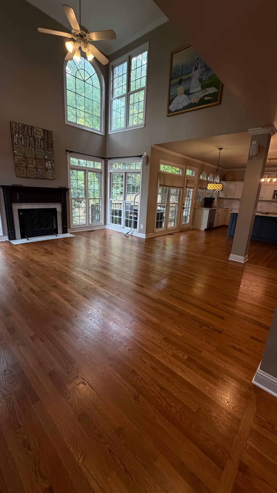 Spacious living room with hardwood floors, tall windows, a fireplace, and a ceiling fan, seen from an open entry.