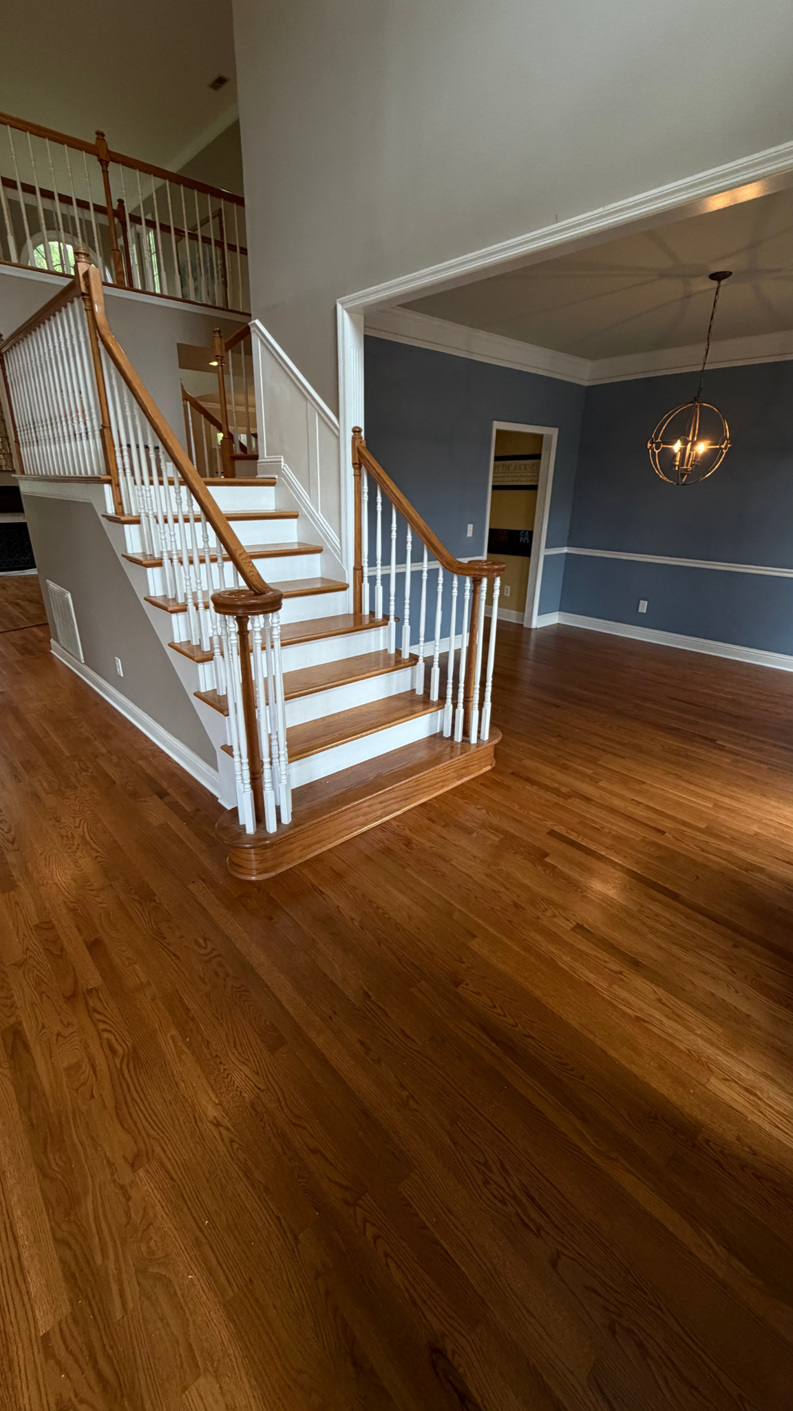 Empty living room with hardwood floors, blue walls, and a white staircase with wooden railings.
