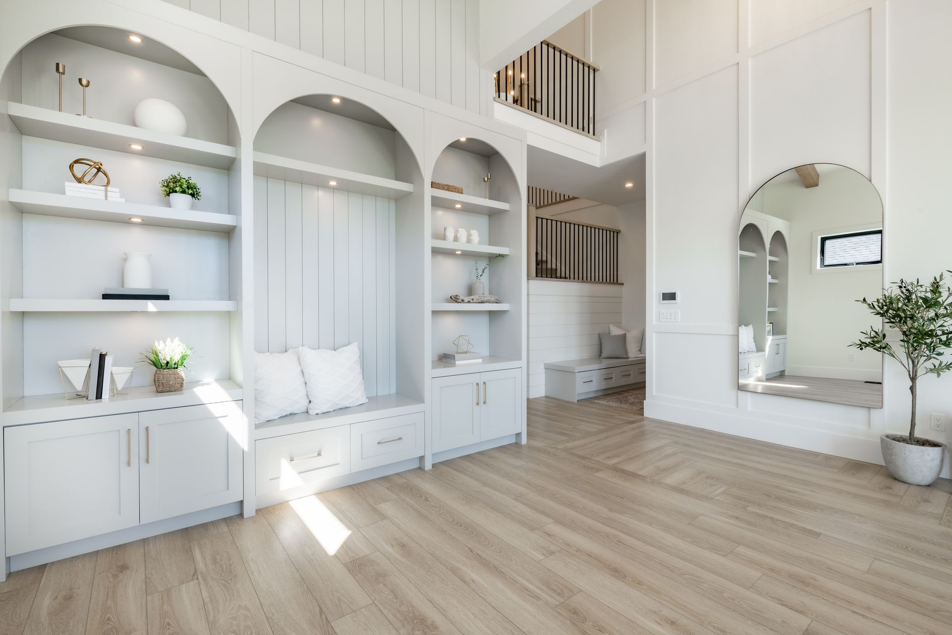 Bright white minimalist room with arched built-in shelving, bench seating, wood floors, and a large mirror