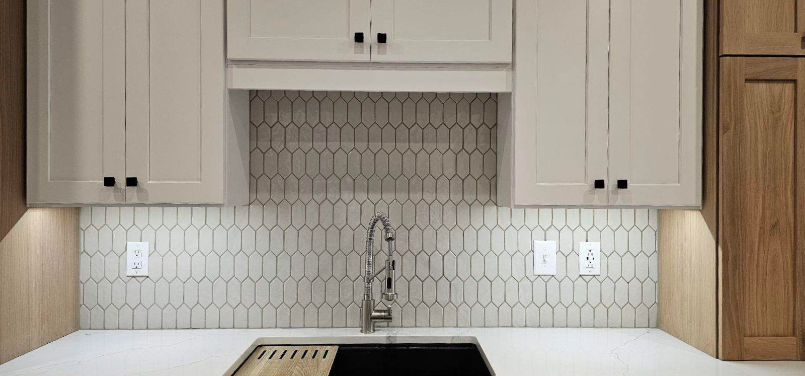 Modern kitchen backsplash with white cabinets, light wood accents, and a black sink under the counter