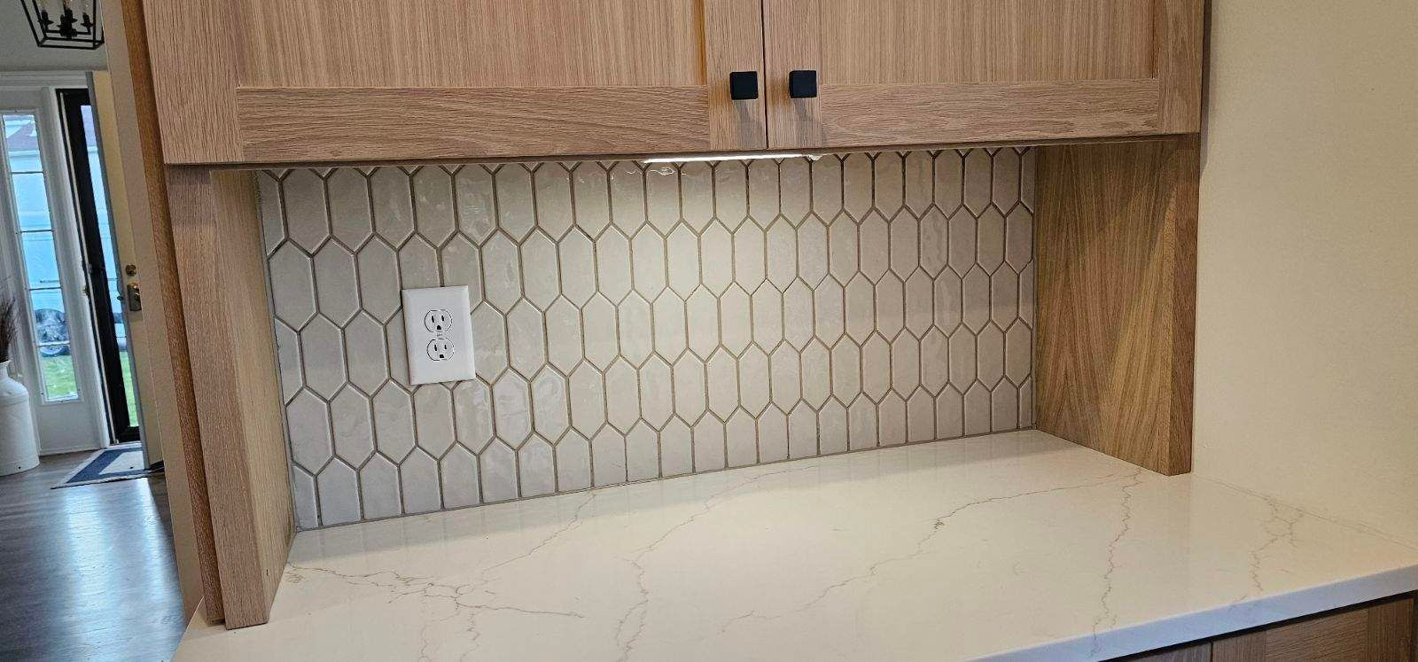 Kitchen alcove with wood cabinets, hex tile backsplash, and a white countertop