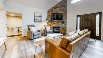 Bright living room with leather sofa, recliner, stone fireplace, and open doorway to dining area