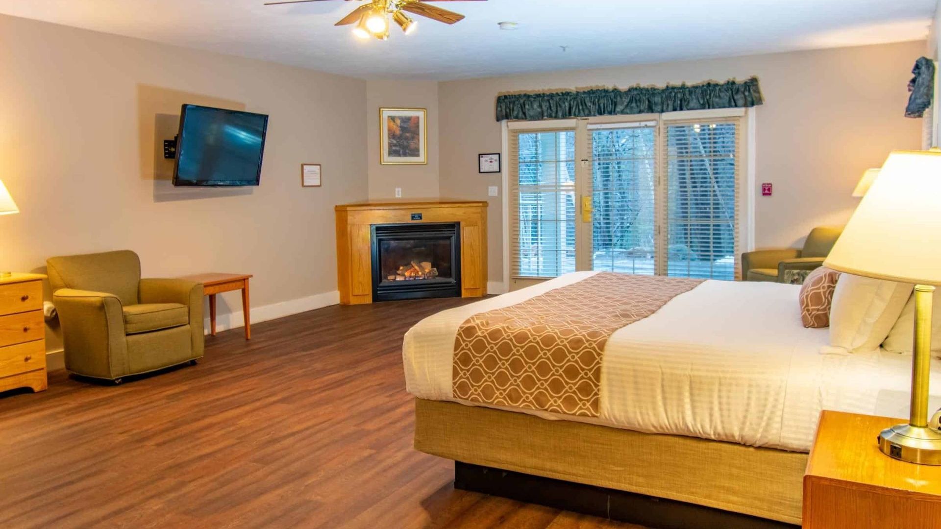 Spacious hotel room with king bed, fireplace, TV, armchair, and sliding doors to a balcony.