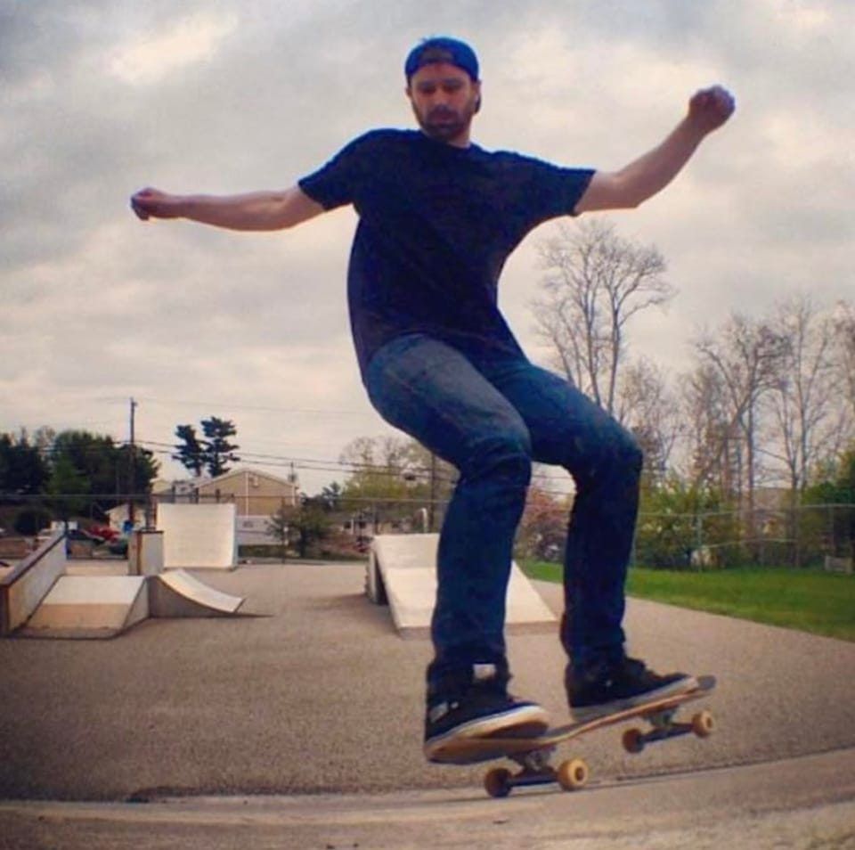 Skateboarder doing a trick at an outdoor skatepark, arms out for balance.