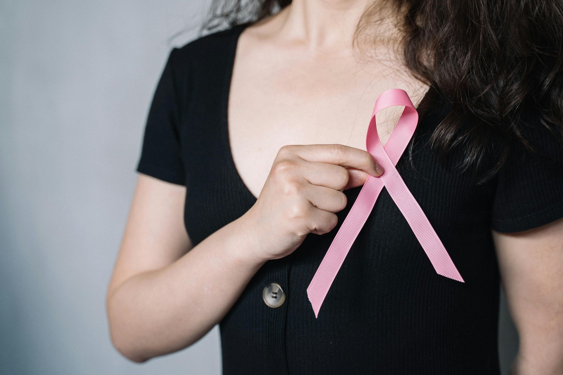 Woman wearing a black shirt, holding a pink breast cancer awareness ribbon.