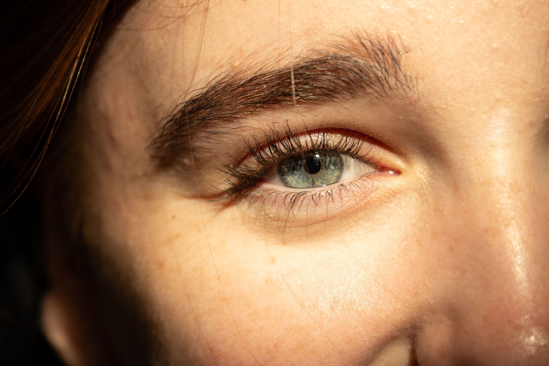 Close-up of a person’s eye and brow in warm sunlight, showing a slight smile.