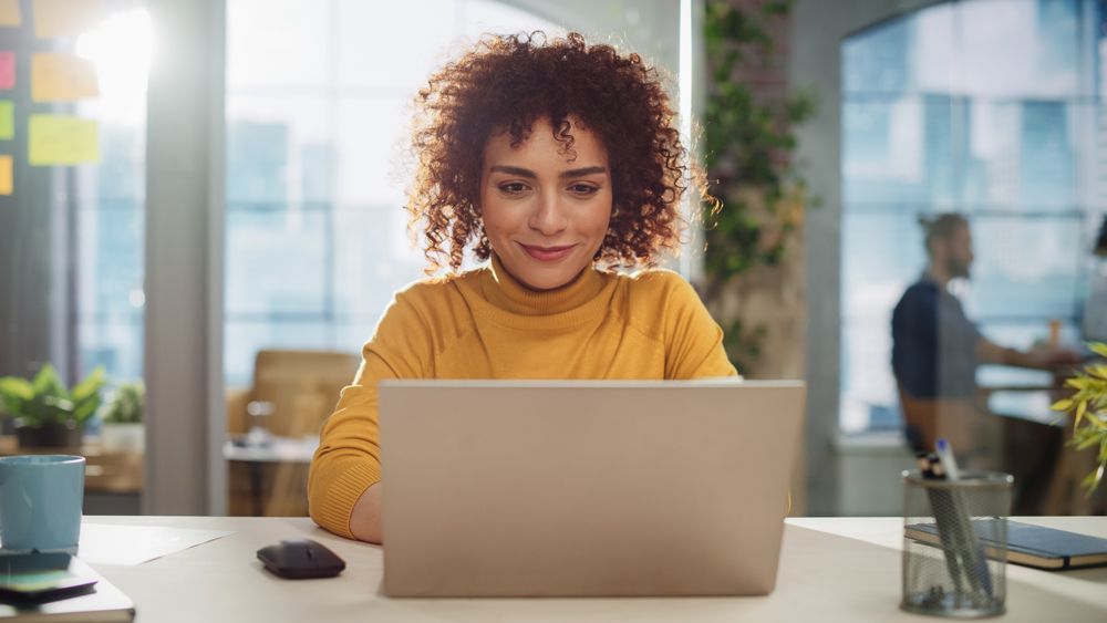 A woman is sitting at a desk using a laptop computer.