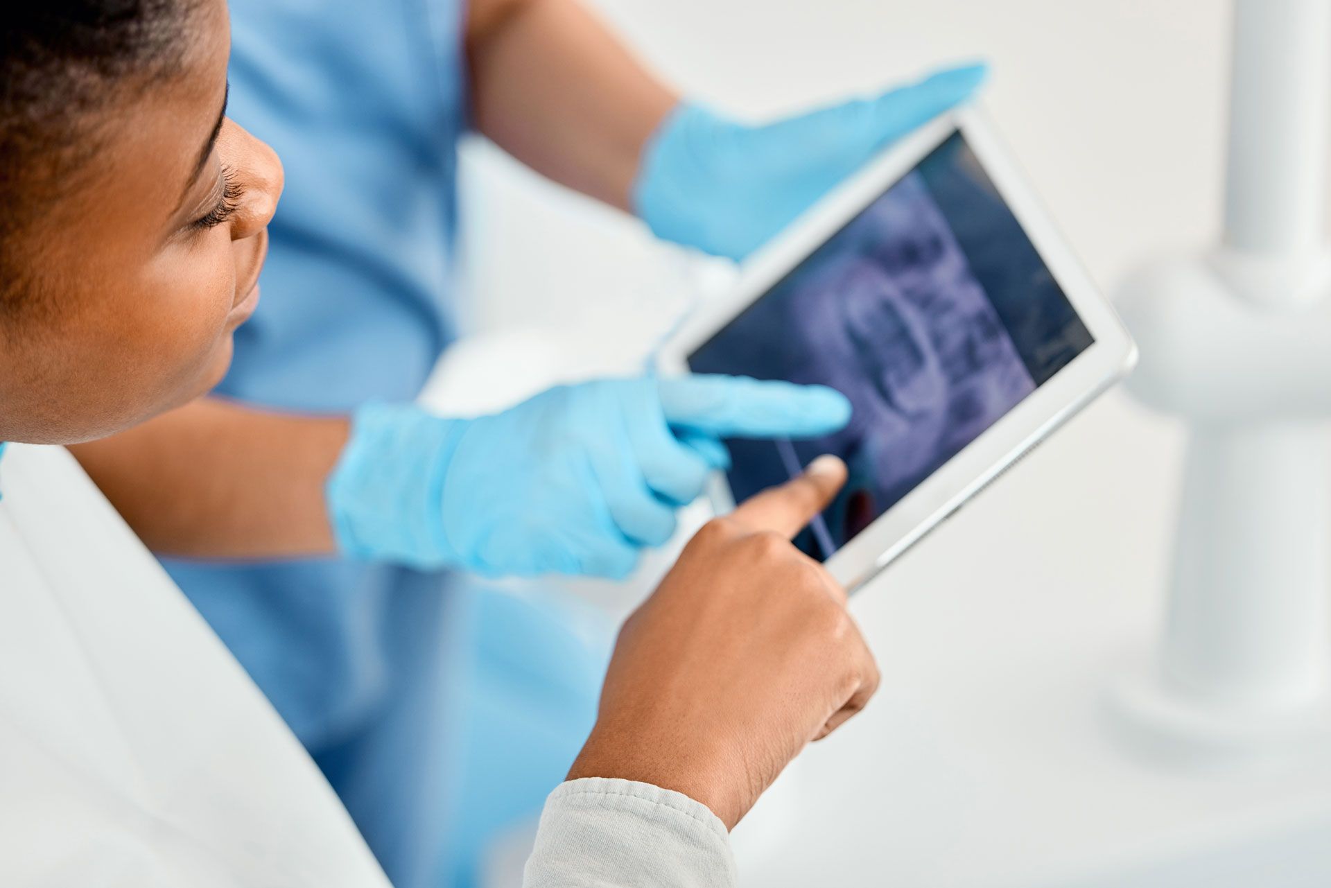 Two medical professionals examine a dental X-ray on a tablet, pointing.