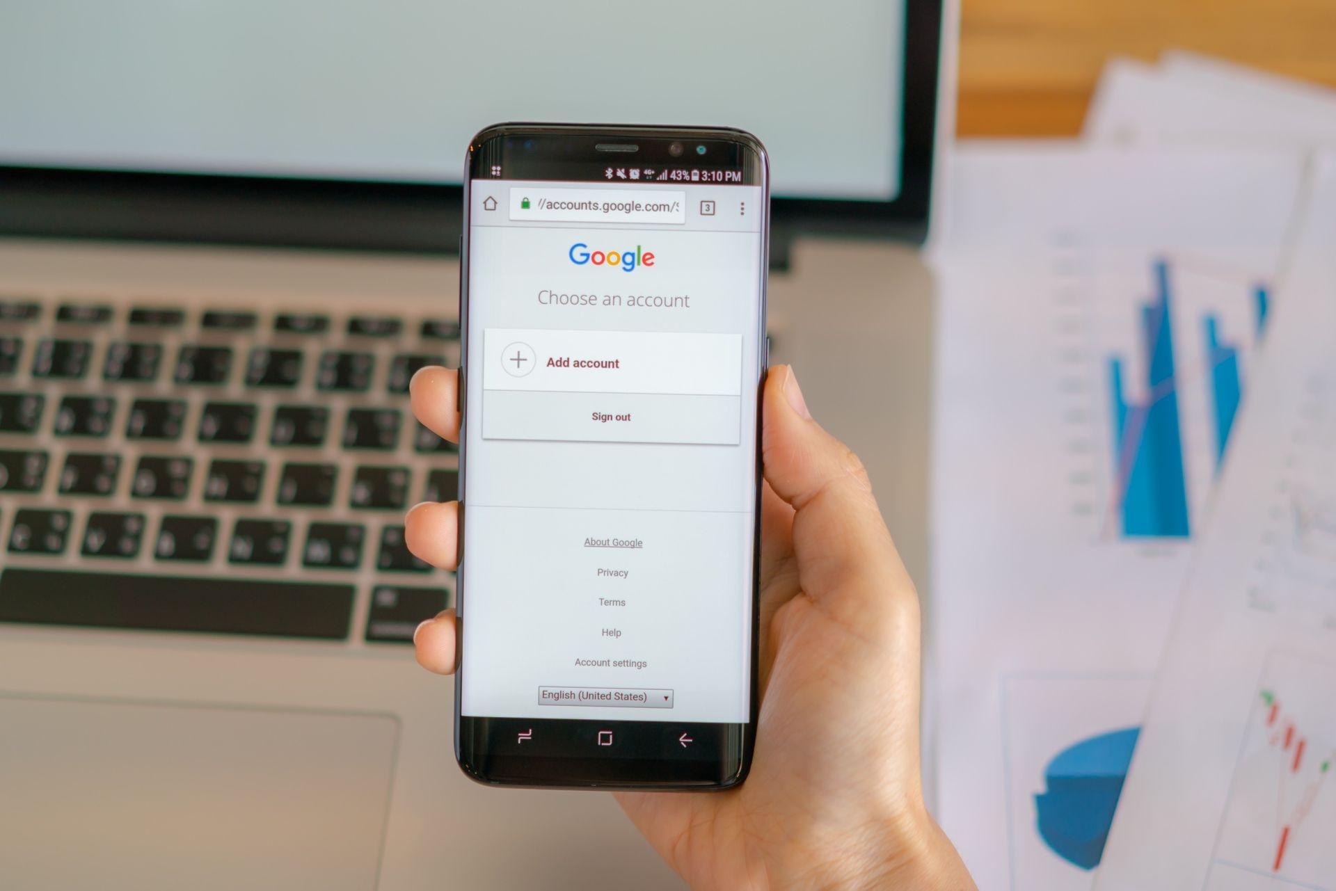 A person is holding a cell phone in front of a laptop.