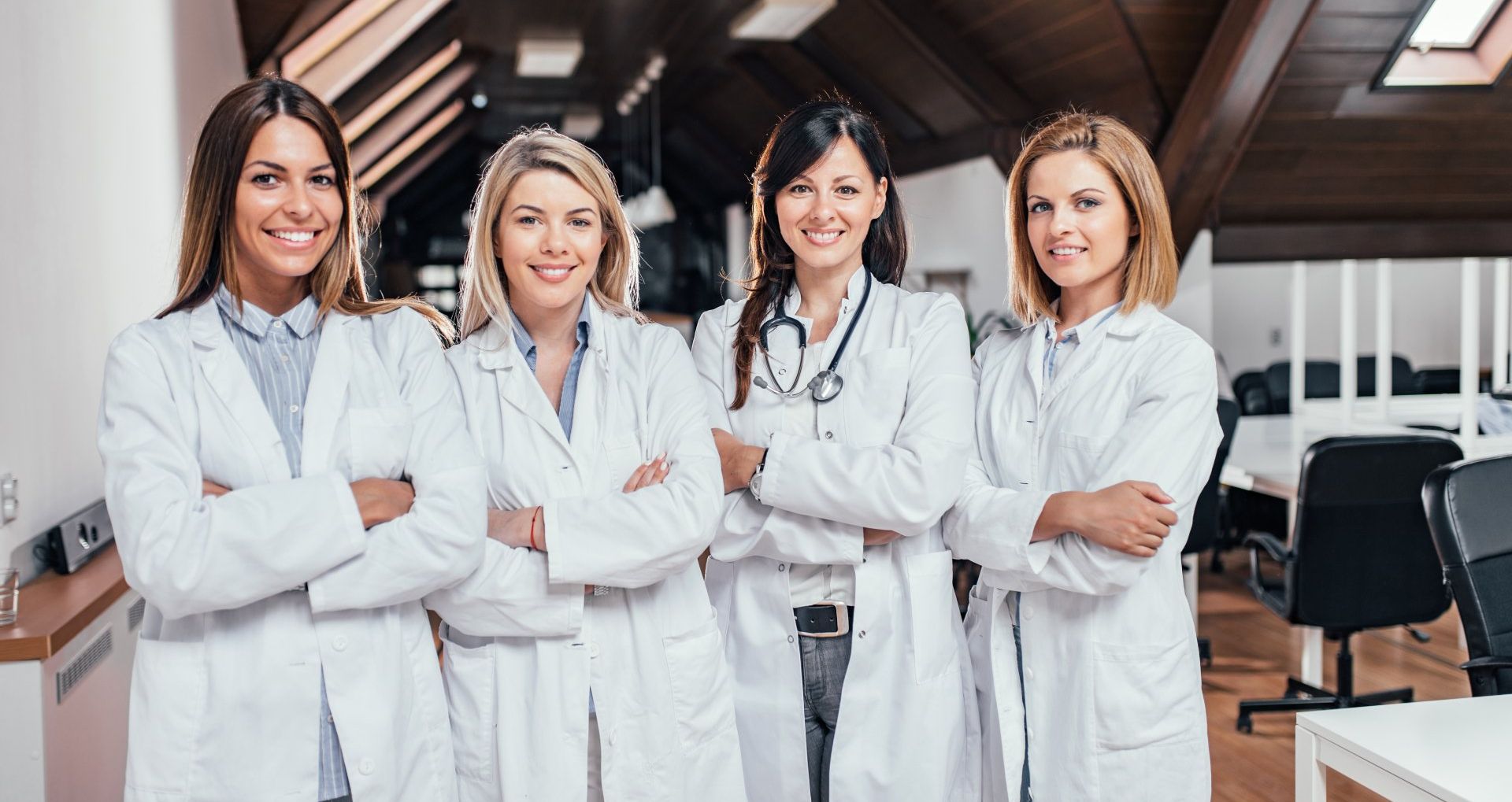 Quatre femmes médecins souriantes en blouse blanche, les bras croisés, dans un bureau.