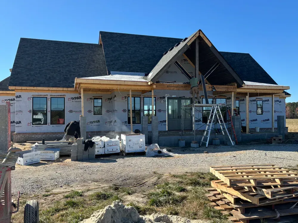 House under construction with scaffolding, ladder, and building materials in front.
