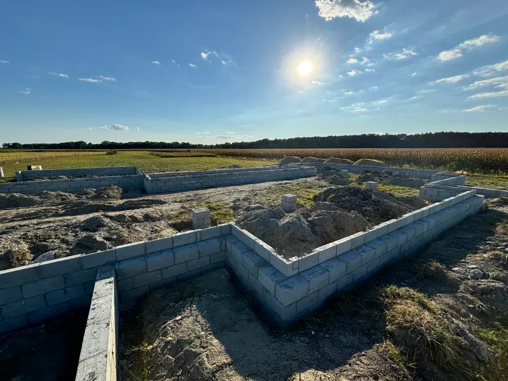 Foundation walls under construction in a grassy field at sunset