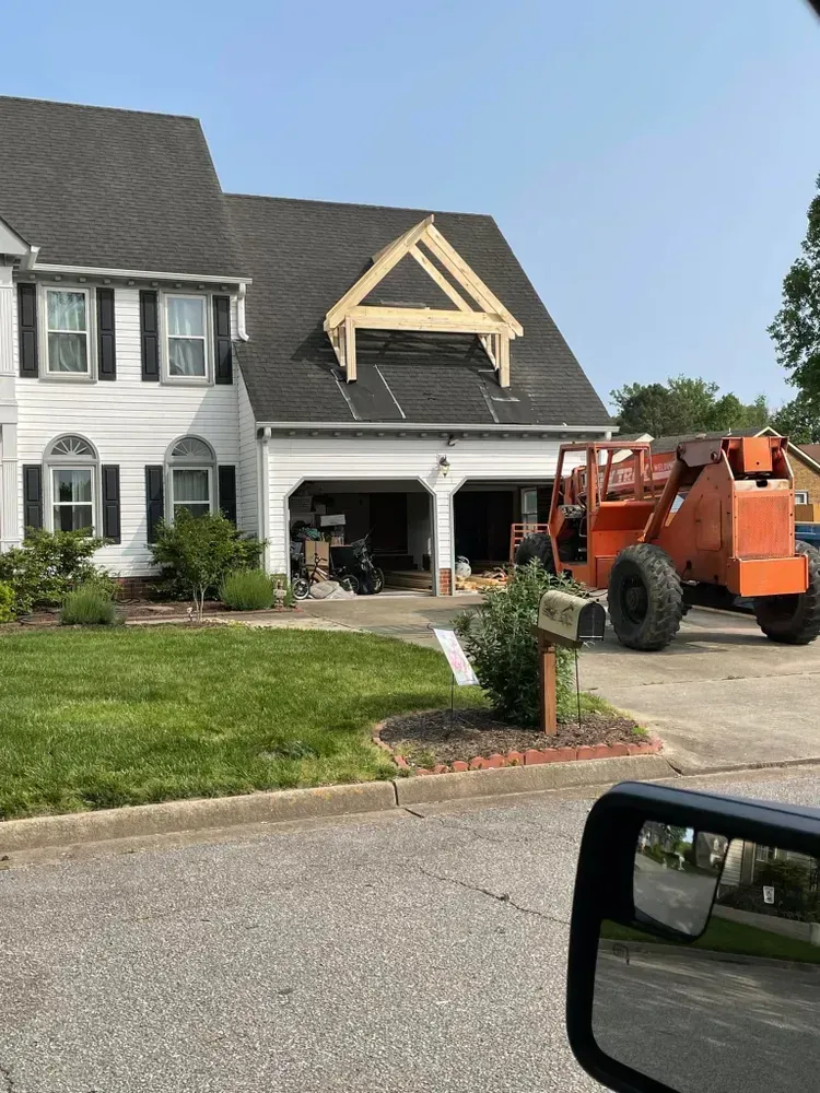 Orange construction lift beside a gray house with new gable framing under the roof.