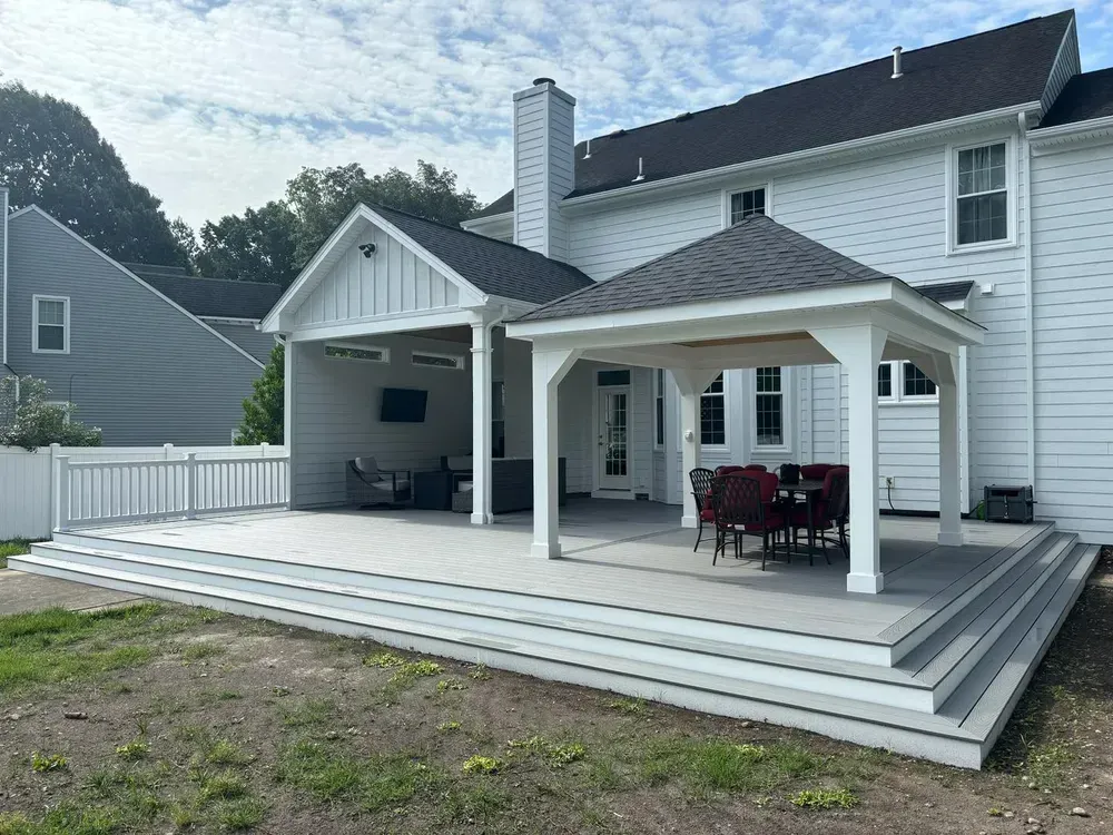 White house with a large covered deck, steps, and patio furniture in a backyard