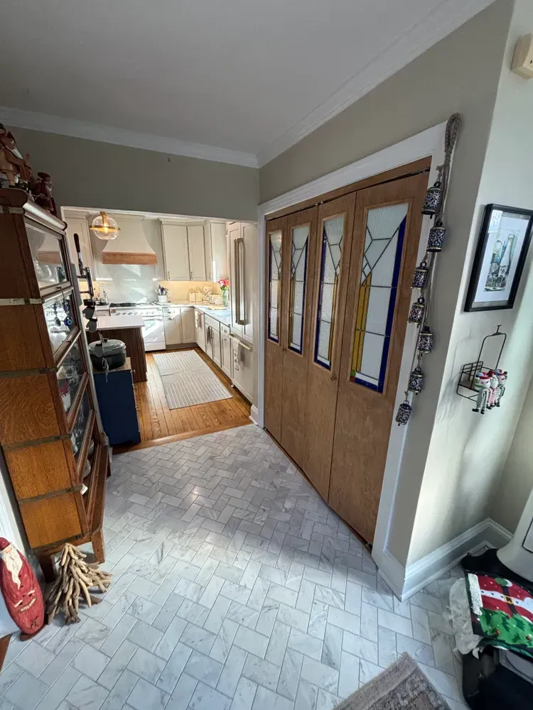 Hallway leading to a bright kitchen, with wooden double doors and tiled floor