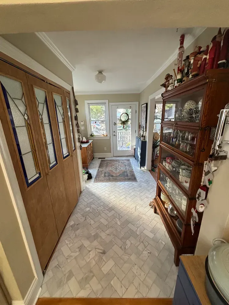 Narrow hallway with tiled floor, wooden cabinets, glass display case, and bright doors at the far end.