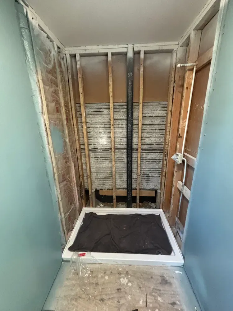 Unfinished bathroom with exposed wall studs, tiled back wall, and a shower base on a dirty floor.