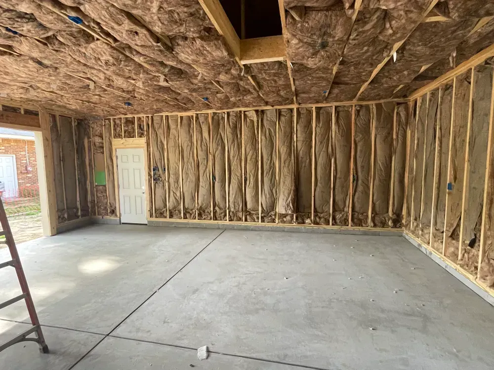 Unfinished garage interior with exposed insulation, concrete floor, ladder, and white door at the back