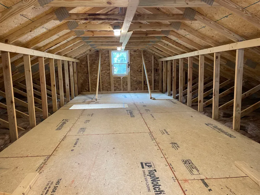 Empty attic framed in wood with plywood flooring and a small window at the far end.