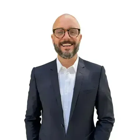 A bald man with a beard and glasses is wearing a suit and smiling.