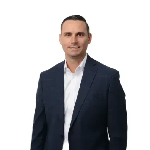 A man in a suit and white shirt is standing in front of a white background.