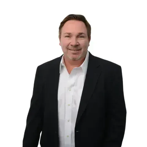 A man in a suit and white shirt is standing in front of a white background.