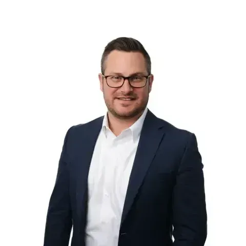 A man in a suit and glasses is standing in front of a white background.