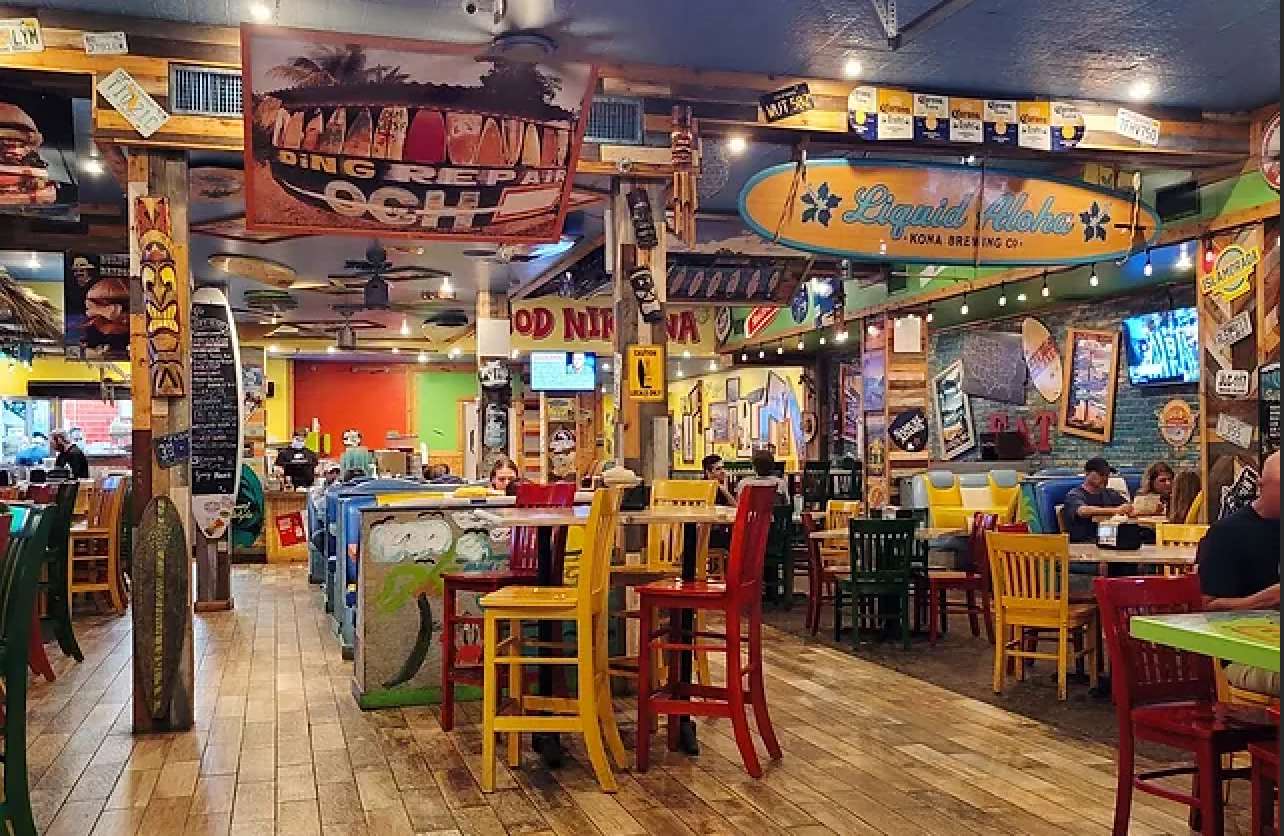 A restaurant with a lot of tables and chairs and a surfboard on the ceiling.