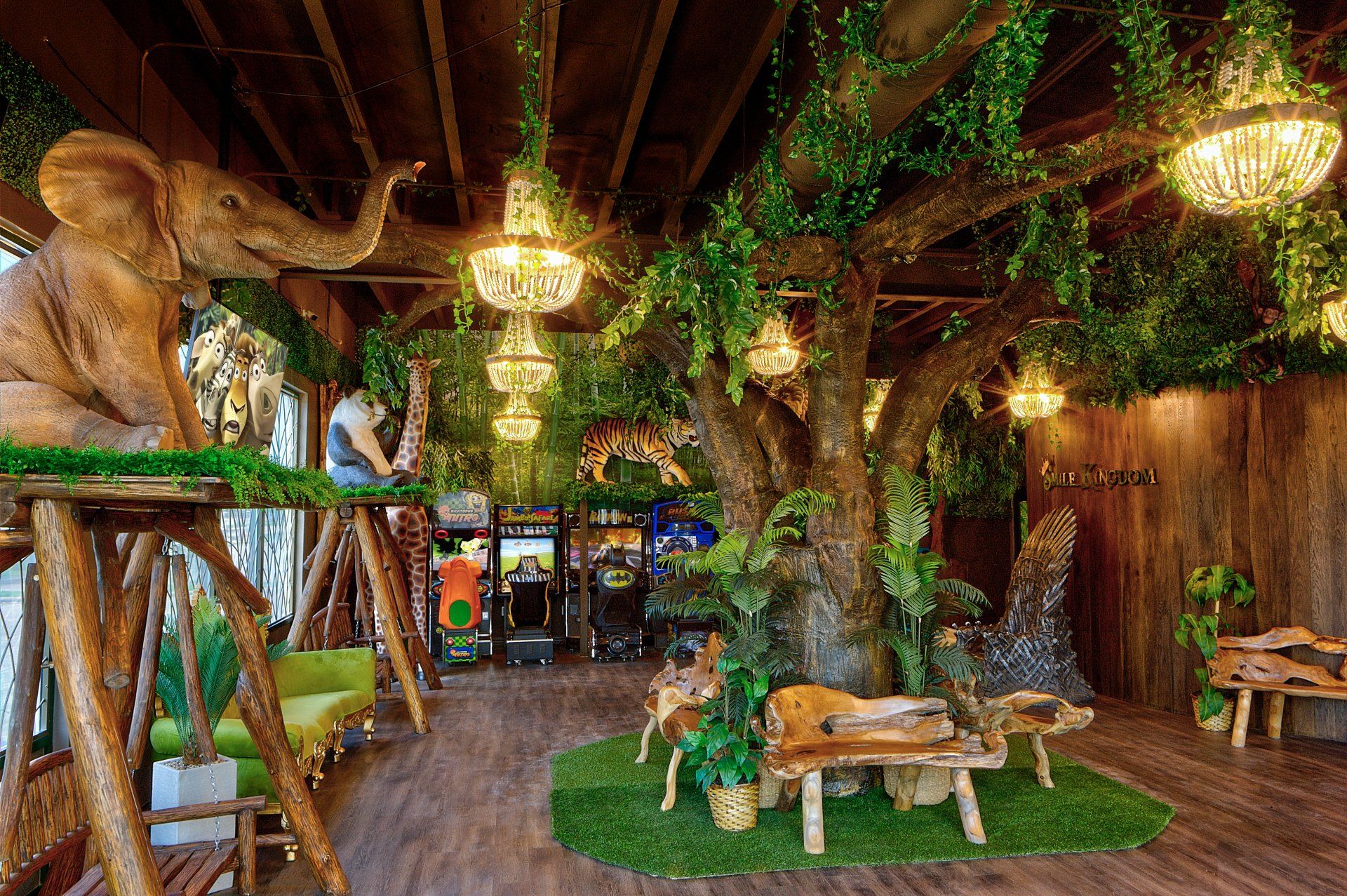 Indoor jungle-themed room with tree trunk decor, hanging lights, and wooden benches on a green turf floor