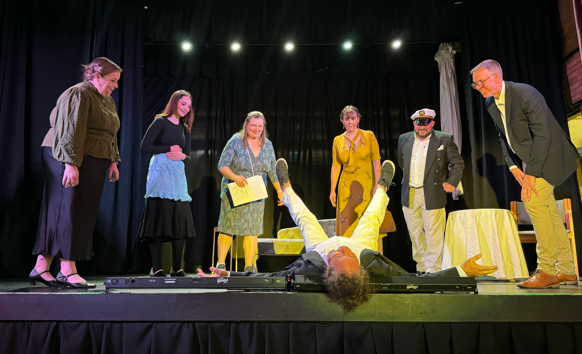 A group of people are standing around a man laying on his back on a stage.